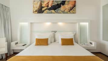 A hotel room with a large bed, two bedside tables, a nightstand, a painting above the bed, and a window with curtains.