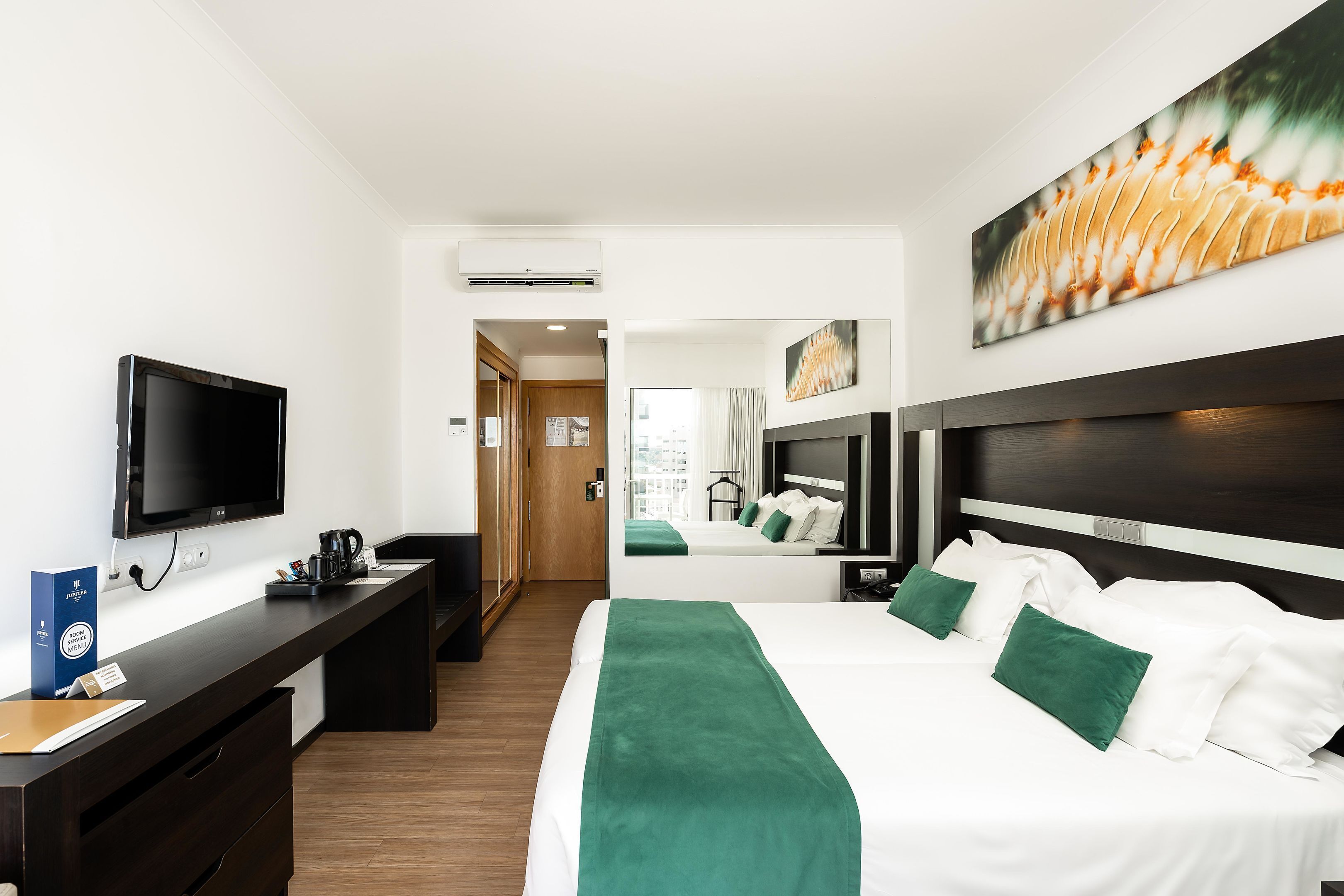 A hotel room with a bed, a desk with a flat-screen TV, a coffee maker, and a large window.