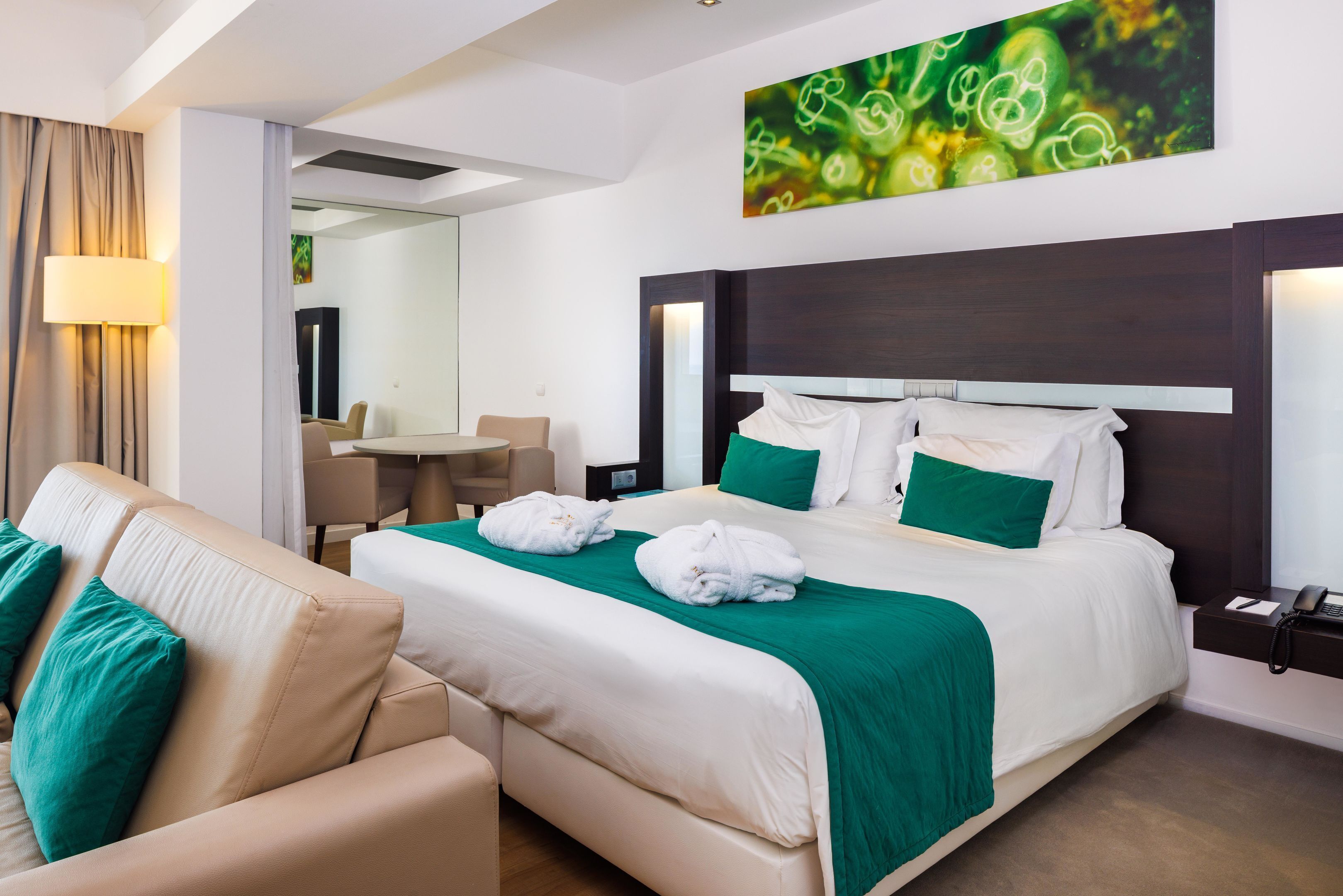 A hotel room with a large bed, a sofa, a desk, and a mirror.