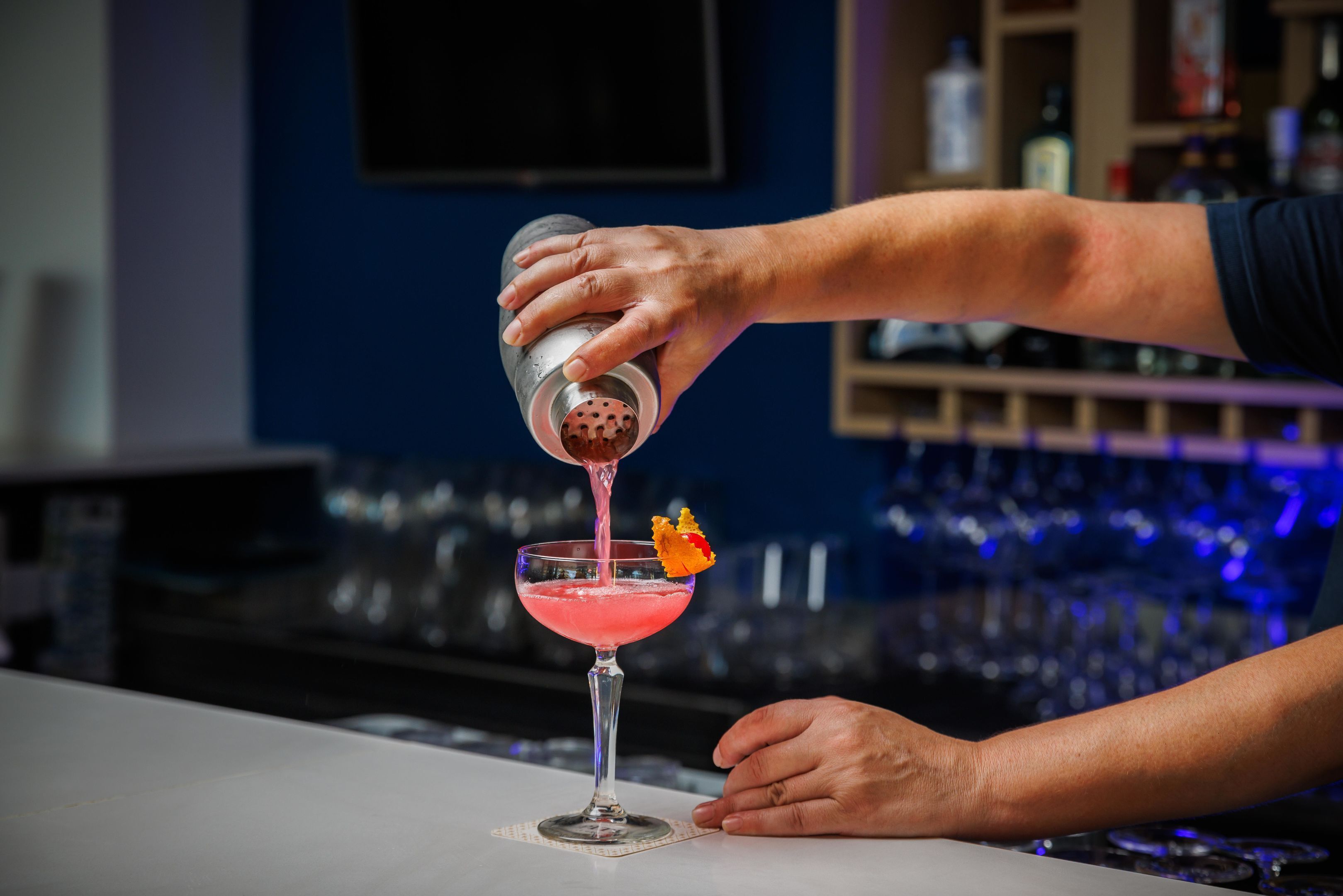 A bartender pouring a pink cocktail into a martini glass with a garnish.