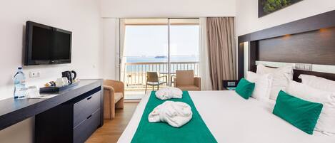 Habitación de hotel con cama, escritorio, televisor, balcón con vistas y un cuadro en la pared.