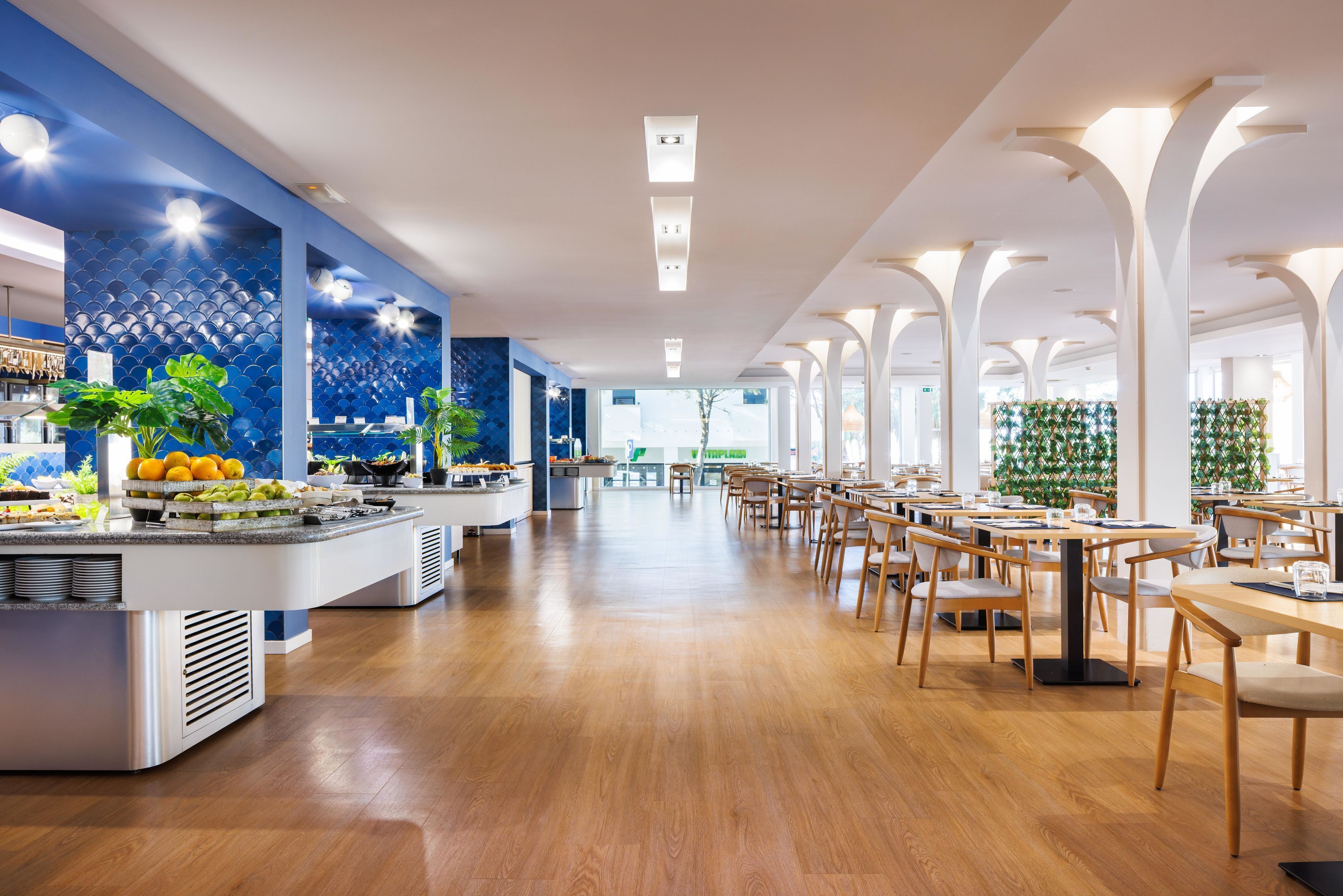 A spacious hotel lobby with a long reception desk, multiple seating areas, and a buffet counter.