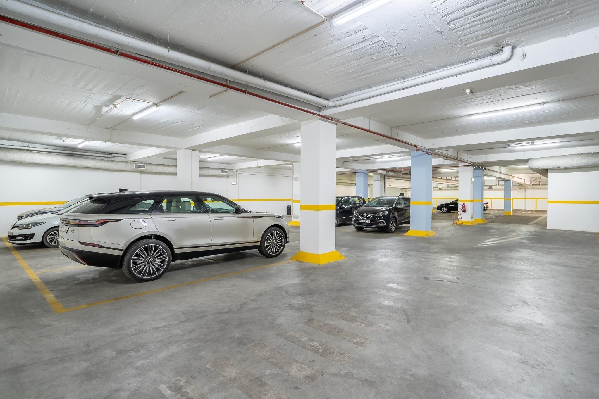 A multi-level underground parking garage with white and yellow pillars, concrete floors, and several parked cars.
