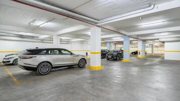 A multi-level underground parking garage with white and yellow pillars, concrete floors, and several parked cars.