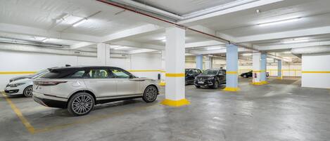 A multi-level underground parking garage with white and yellow pillars, concrete floors, and several parked cars.