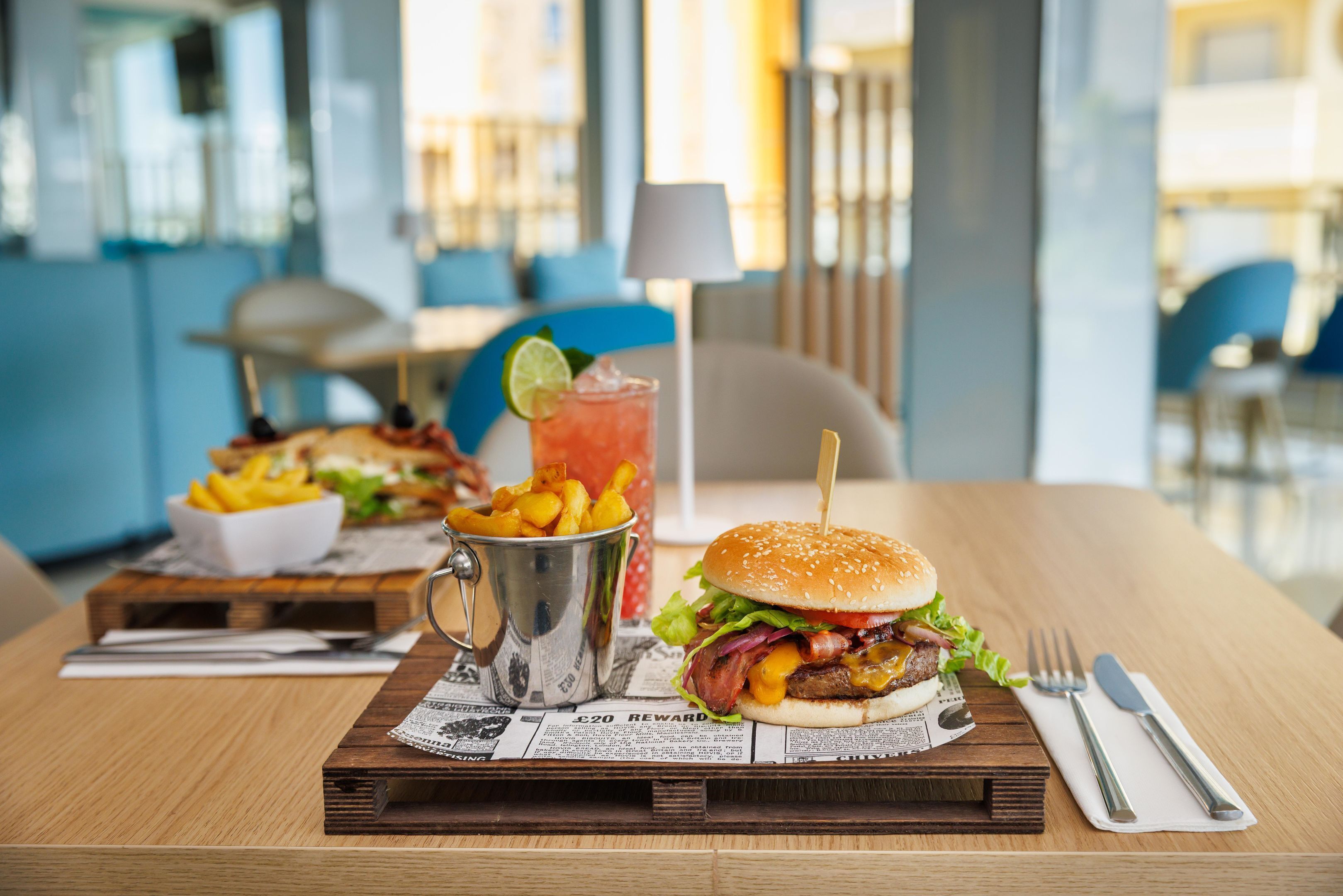 A dining table with a burger, fries, and a drink.