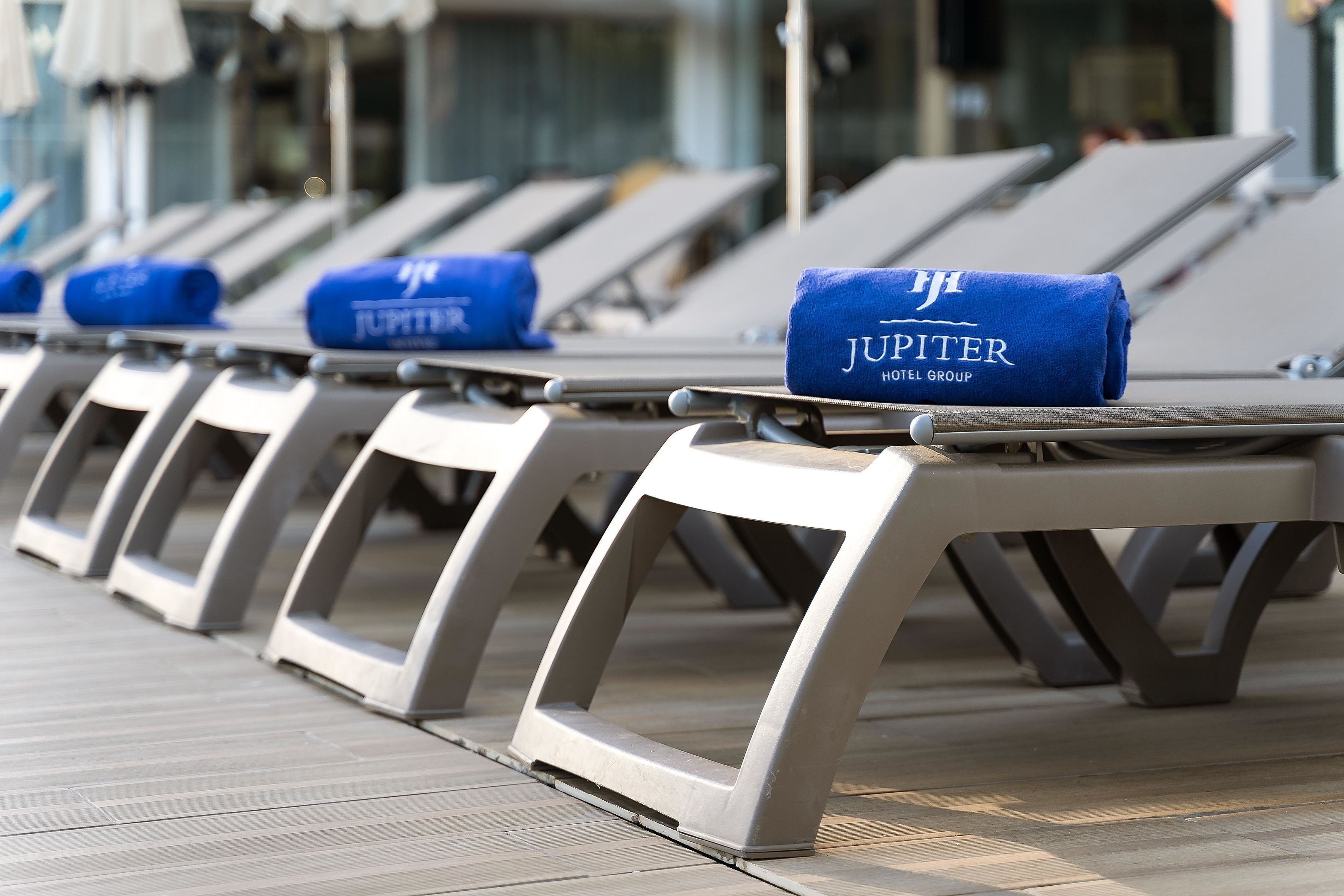 A row of sun loungers with towels labeled "JUPITER HOTEL GROUP" on a wooden deck.