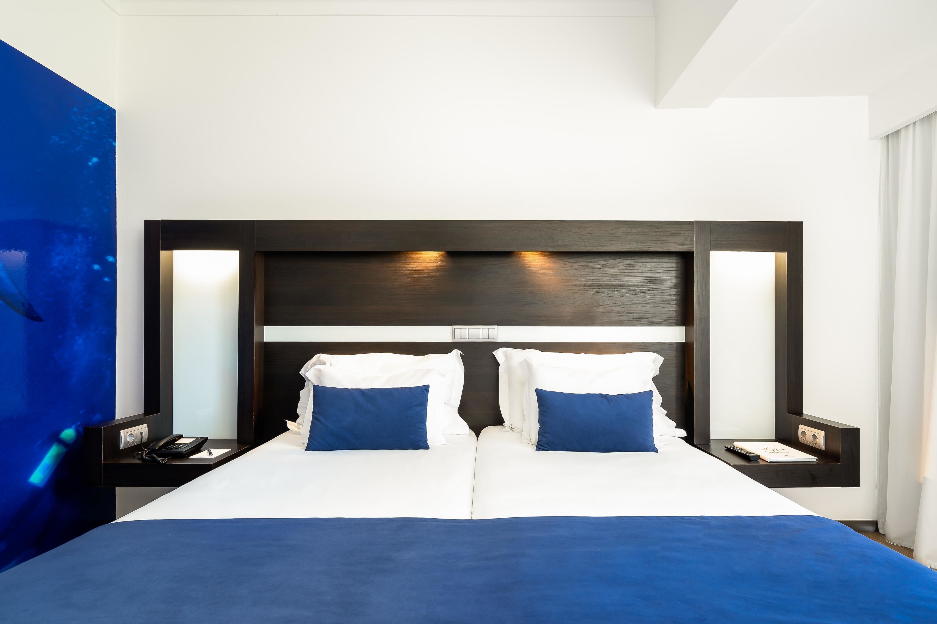 Habitació d'hotel amb un llit gran, dues taules de nit i una paret amb un toc blau.