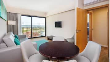 Een moderne woonkamer met een ronde tafel, witte leren banken, een aan de muur bevestigde televisie en een balkon met uitzicht op de stad.
