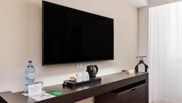 Quarto de hotel com televisão de tela plana na parede, cafeteira, uma garrafa de água e uma pequena mesa com etiqueta de nome.
