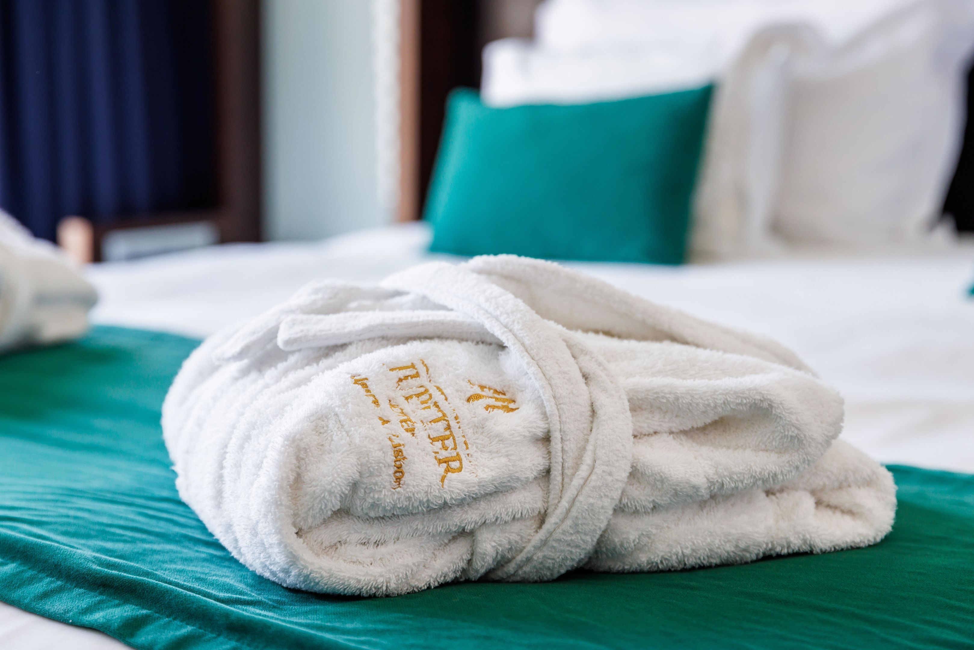 A neatly folded white bathrobe on a bed with teal bedding.