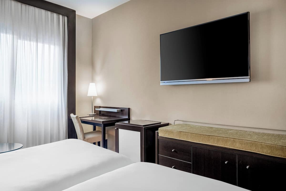 Une chambre d’hôtel avec deux lits, un bureau, une chaise, une télévision et une armoire.