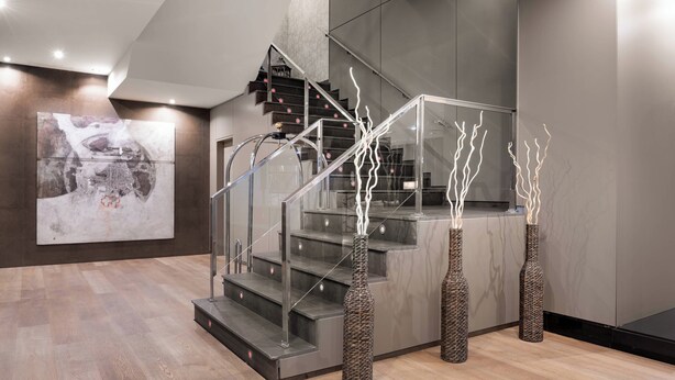 A modern staircase with glass railings, a minimalist design, and three decorative vases with branches.