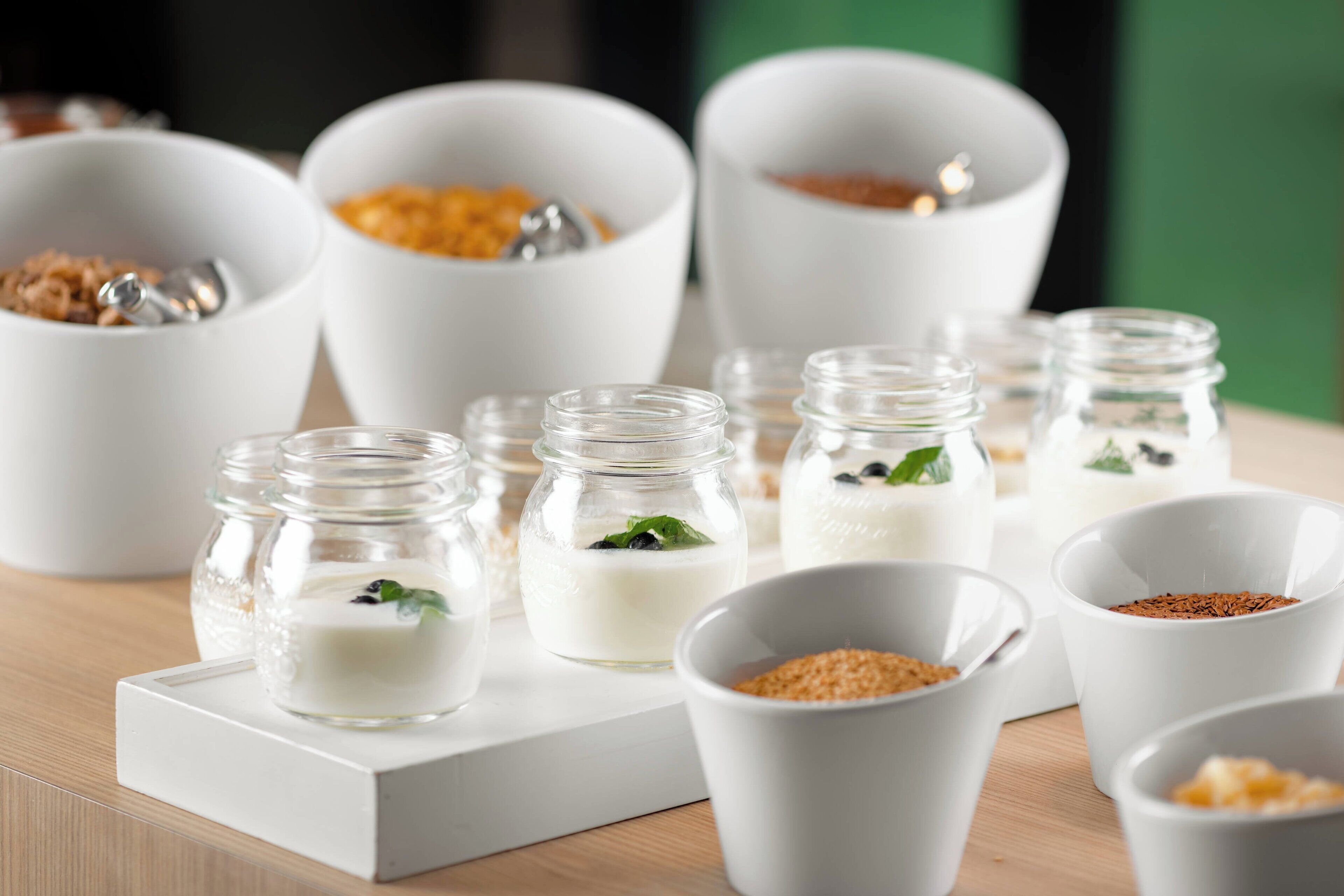 Diversos recipientes blancos, tazones y frascos con distintos alimentos sobre una superficie de madera.