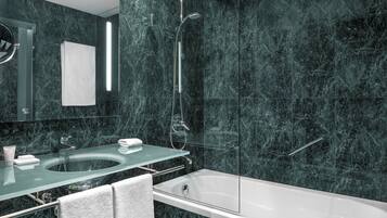 A modern bathroom with a glass-enclosed shower, a white bathtub, and a marble-tiled wall.