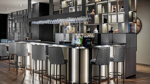 A modern bar area with a central island, bar stools, and a variety of bottles and glasses on shelves.