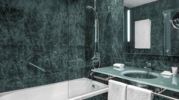 Un baño moderno con bañera de hidromasaje con mampara de vidrio, tocador de vidrio con lavamanos y un espejo grande.