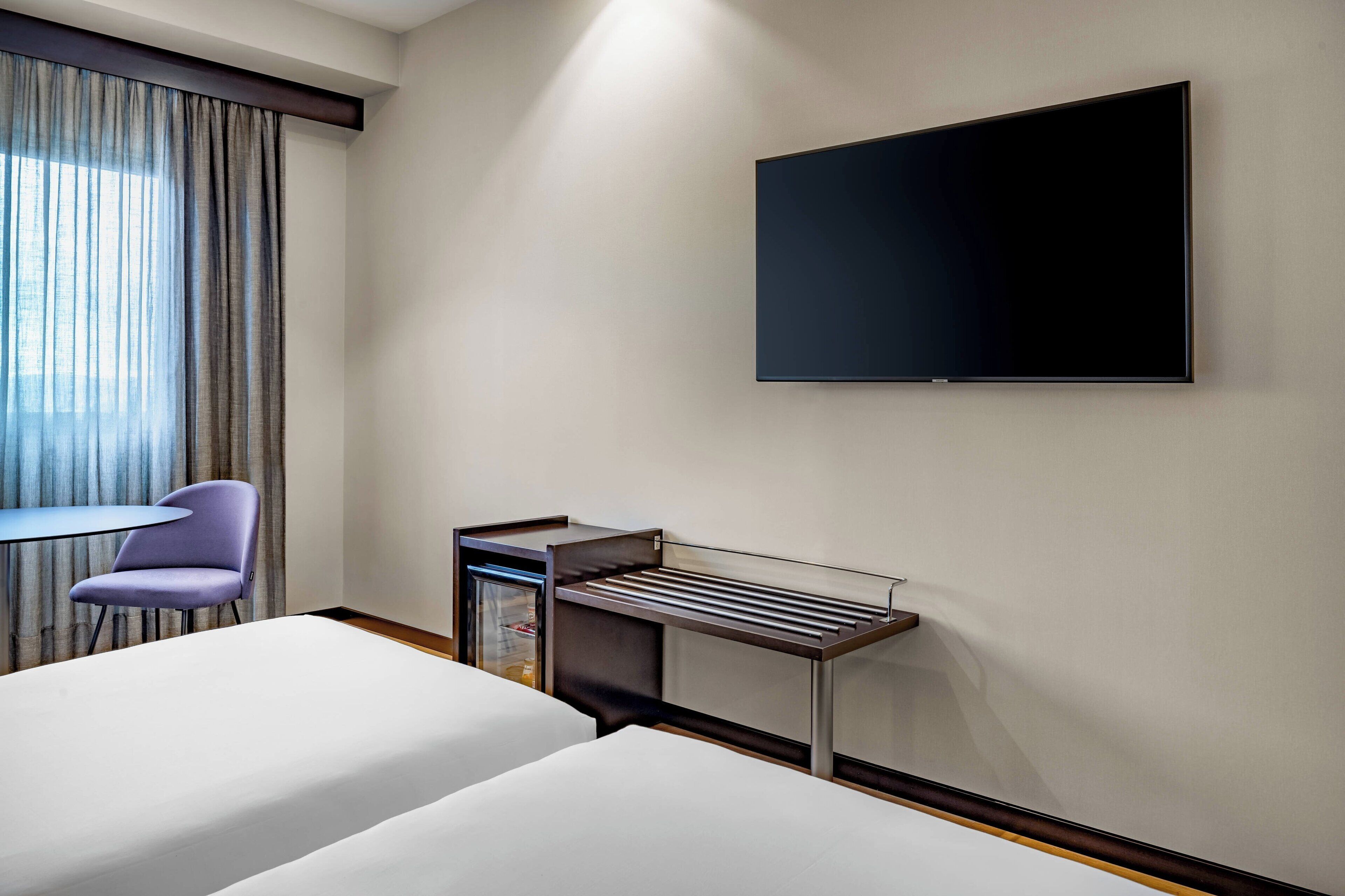 Habitación de hotel con dos camas, un escritorio, una silla, un televisor y una ventana con cortinas.