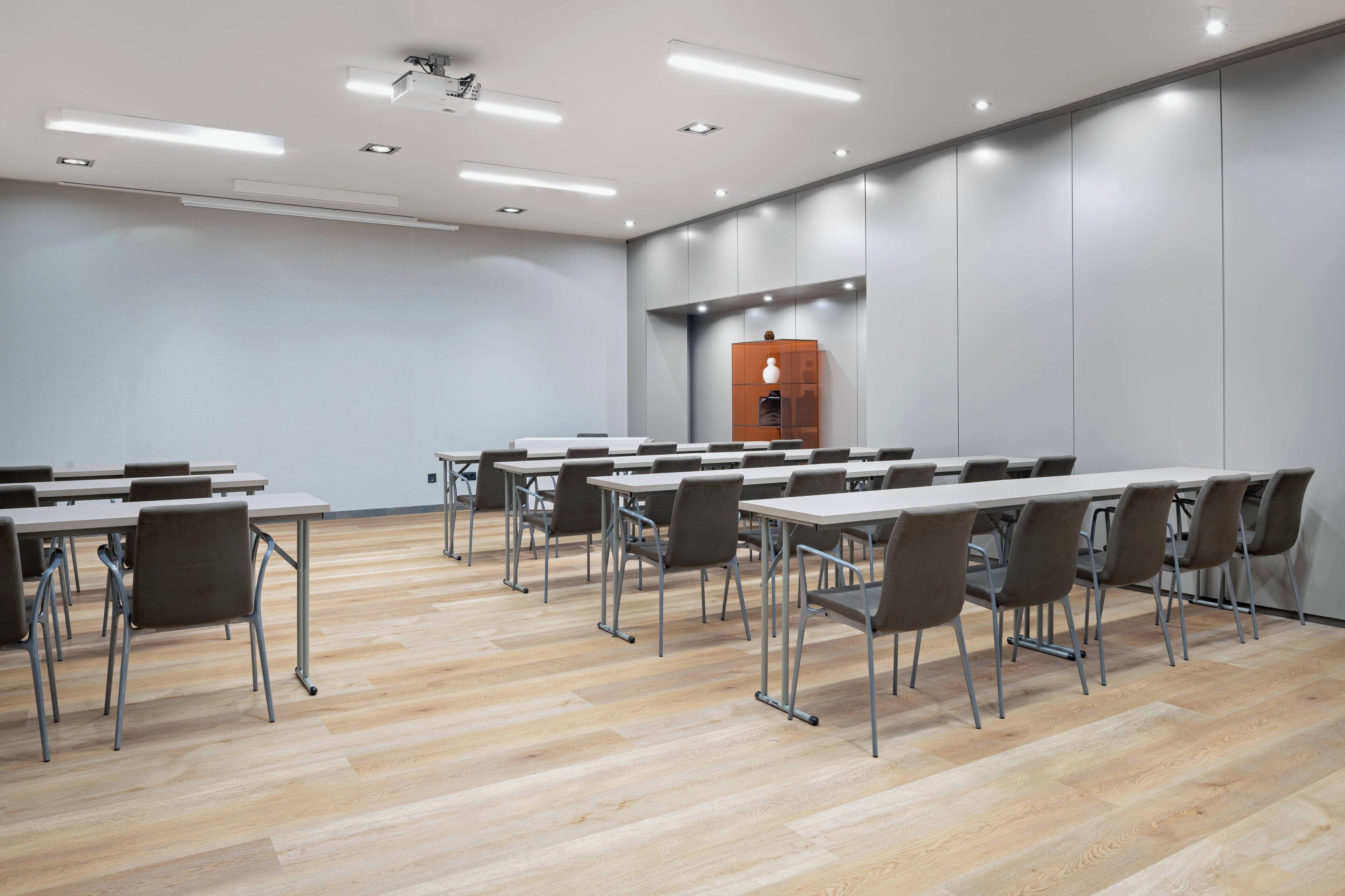 Un salón de conferencias con varias mesas y sillas, piso de madera y un techo moderno con iluminación empotrada.
