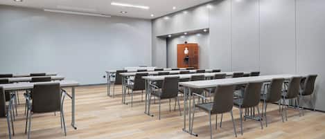 A conference room with multiple tables and chairs, a wooden floor, and a modern ceiling with recessed lighting.