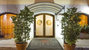 Entrada de hotel con puertas dobles, felpudo con el logotipo del hotel y dos macetas a cada lado.
