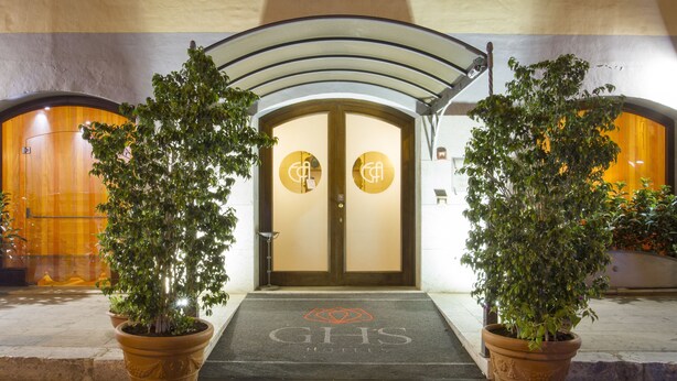 A hotel entrance with a double door, a doormat with the hotel's logo, and two potted plants on either side. - Hotel Vecchio Borgo (Palermo)