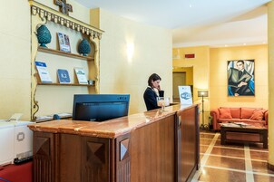 Una reception con un computer, una macchina del caffè e un bicchiere d'acqua. C'è un divano e un quadro appeso al muro.