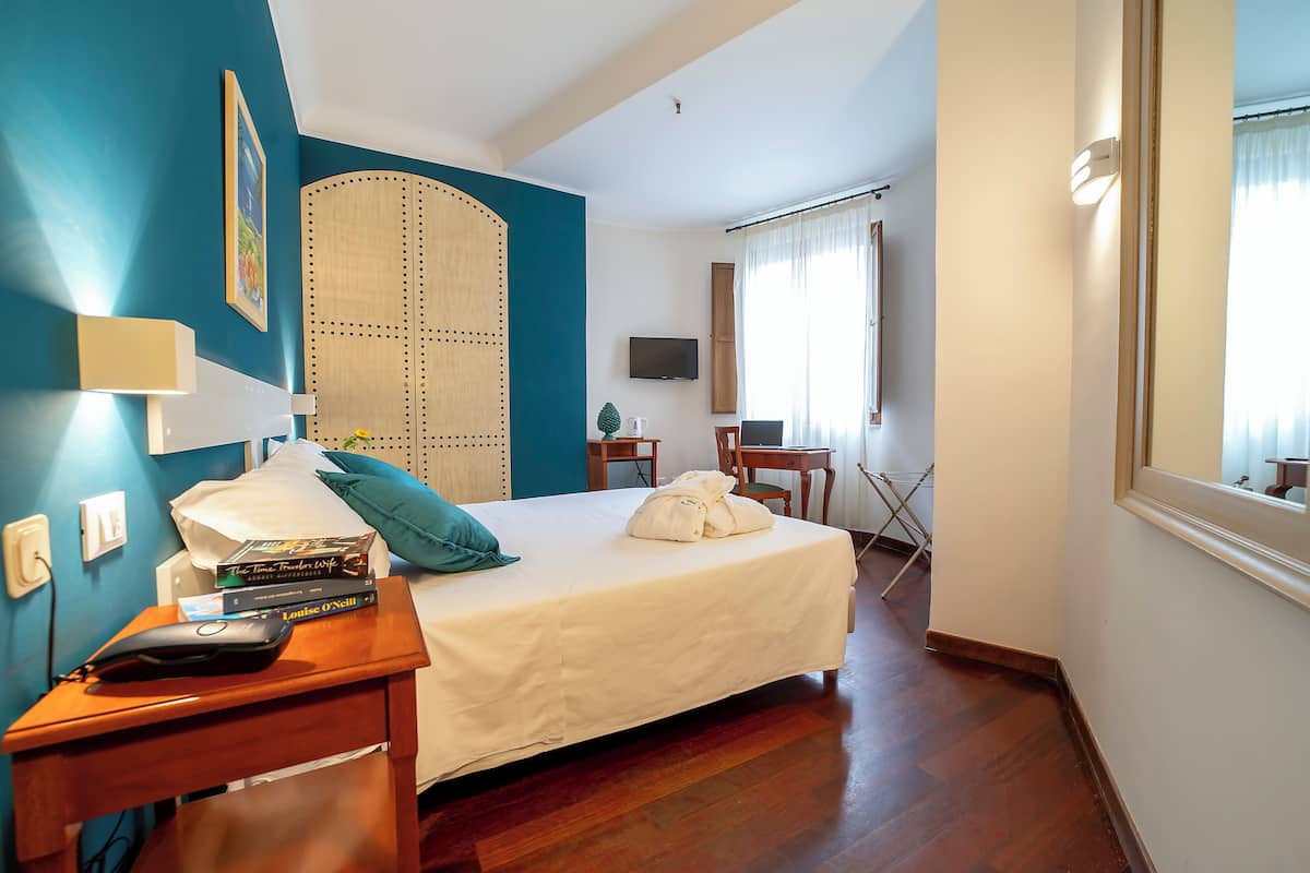A hotel room with a bed, bedside table, a desk with a chair, a TV, and a window with curtains.