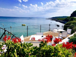 A terrace with a view of the sea, outdoor seating, and red flowers.