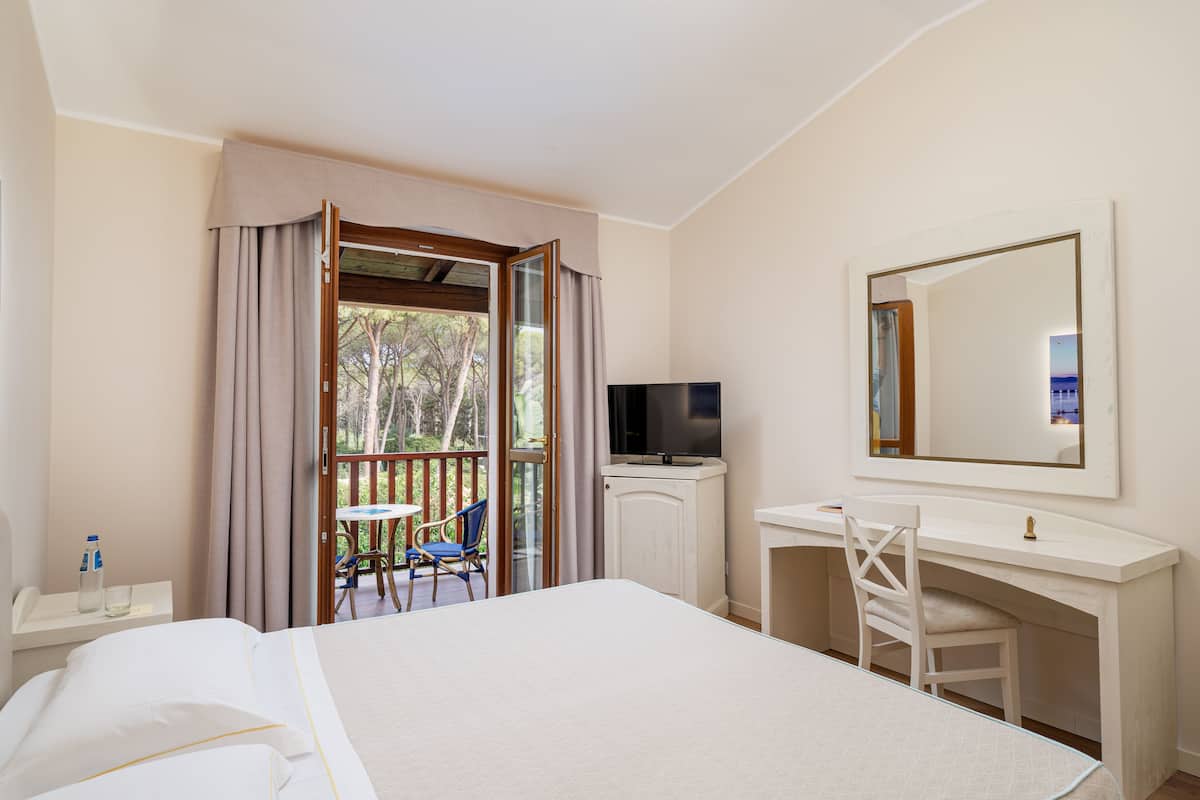 A hotel room with a bed, a desk, a chair, a TV, and a balcony with a table and chairs.