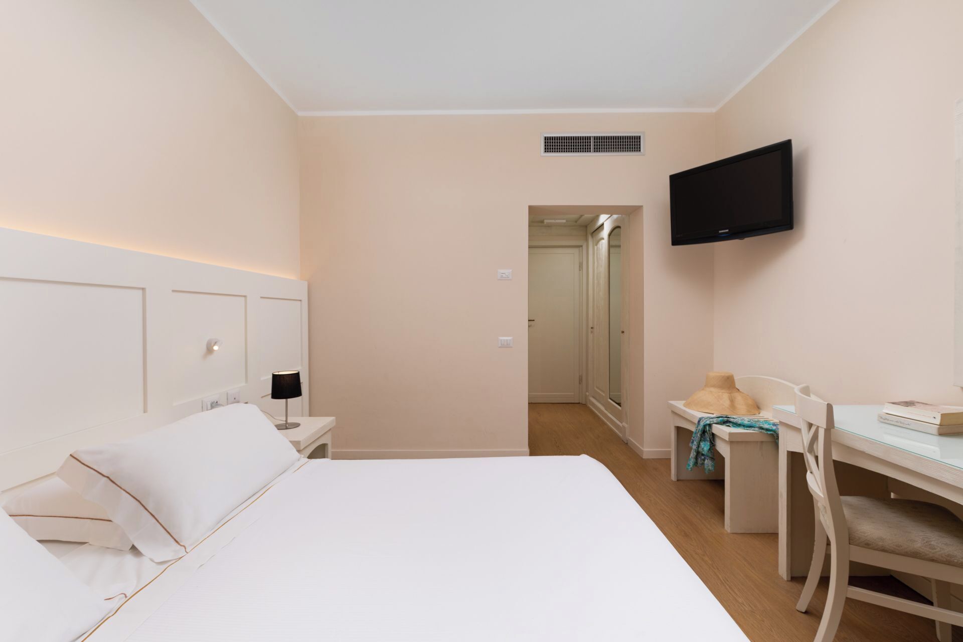 Habitación de hotel con cama, escritorio, silla, televisión y puerta al baño.