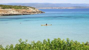 A coastal scene with a person paddling a canoe.