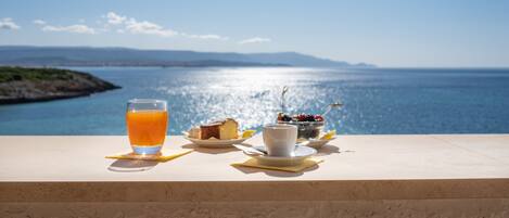 A table with a glass of orange juice, a cup of coffee, and a bowl of berries, overlooking a scenic coastal view.