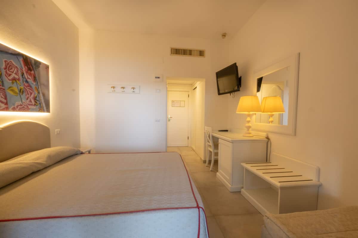 A hotel room with a bed, a desk, a chair, a TV, and a lamp.