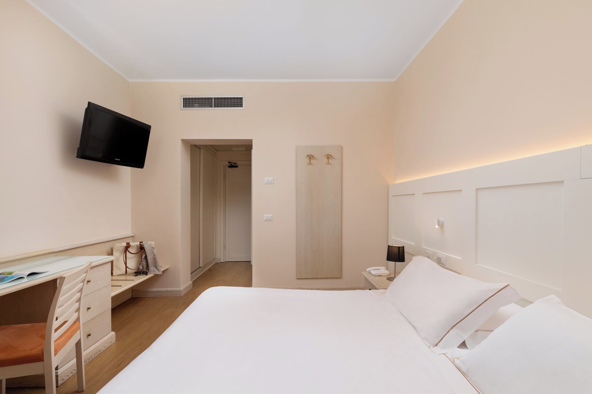 A hotel room with a bed, a desk, a chair, a television, a wardrobe, and a bathroom door.
