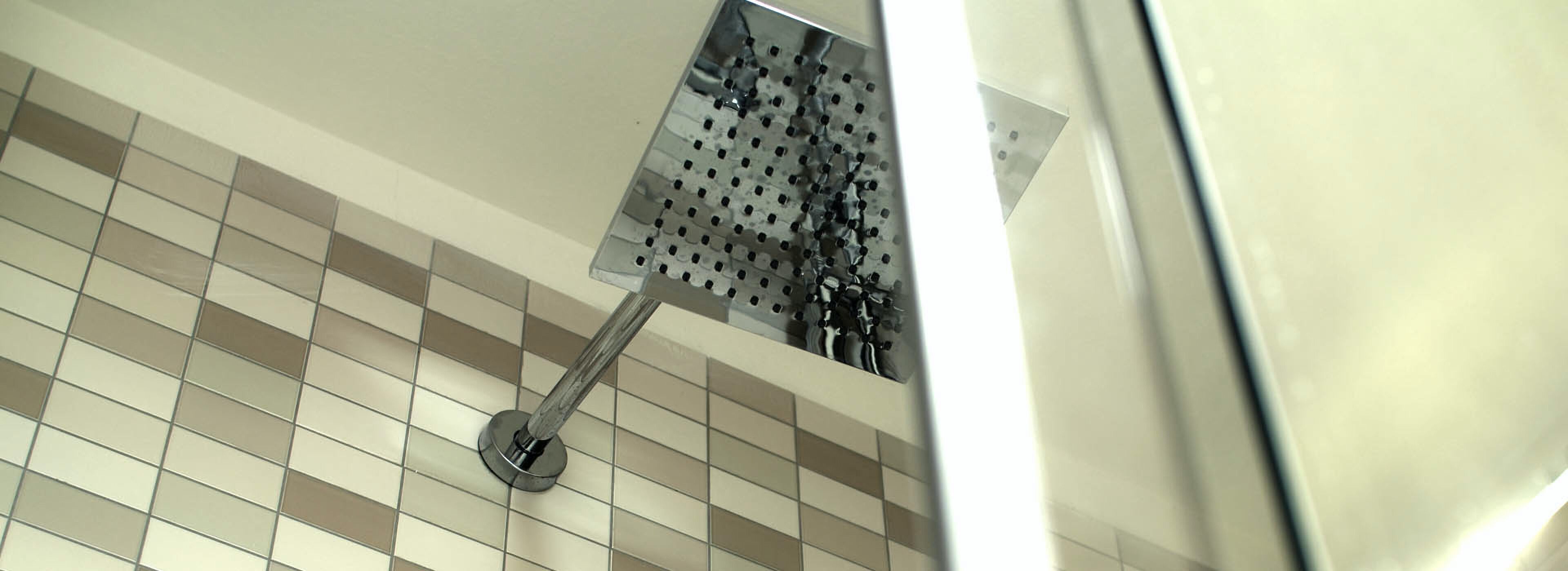 A showerhead with a perforated design, mounted on a tiled wall with a checkered pattern.