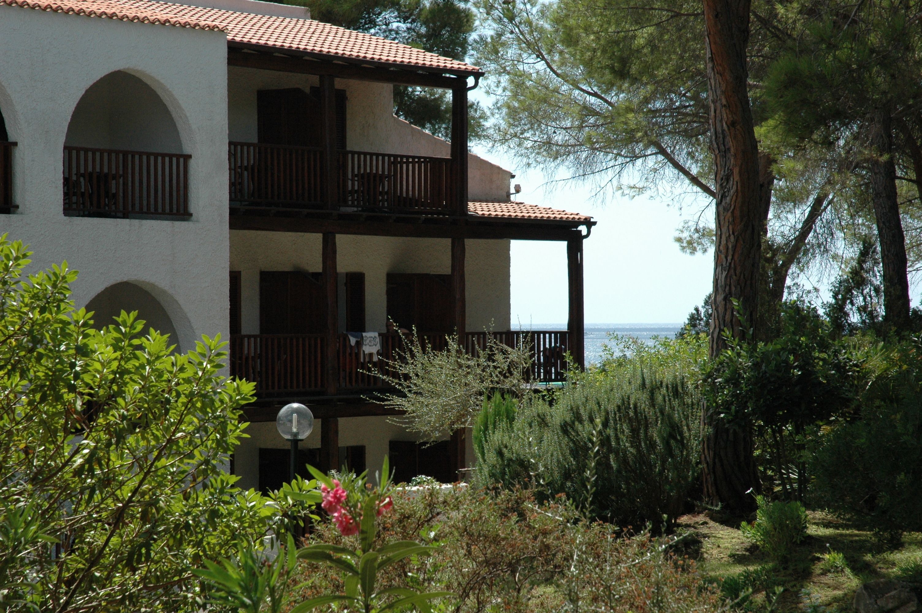 A two-story building with balconies, surrounded by greenery and overlooking a body of water.