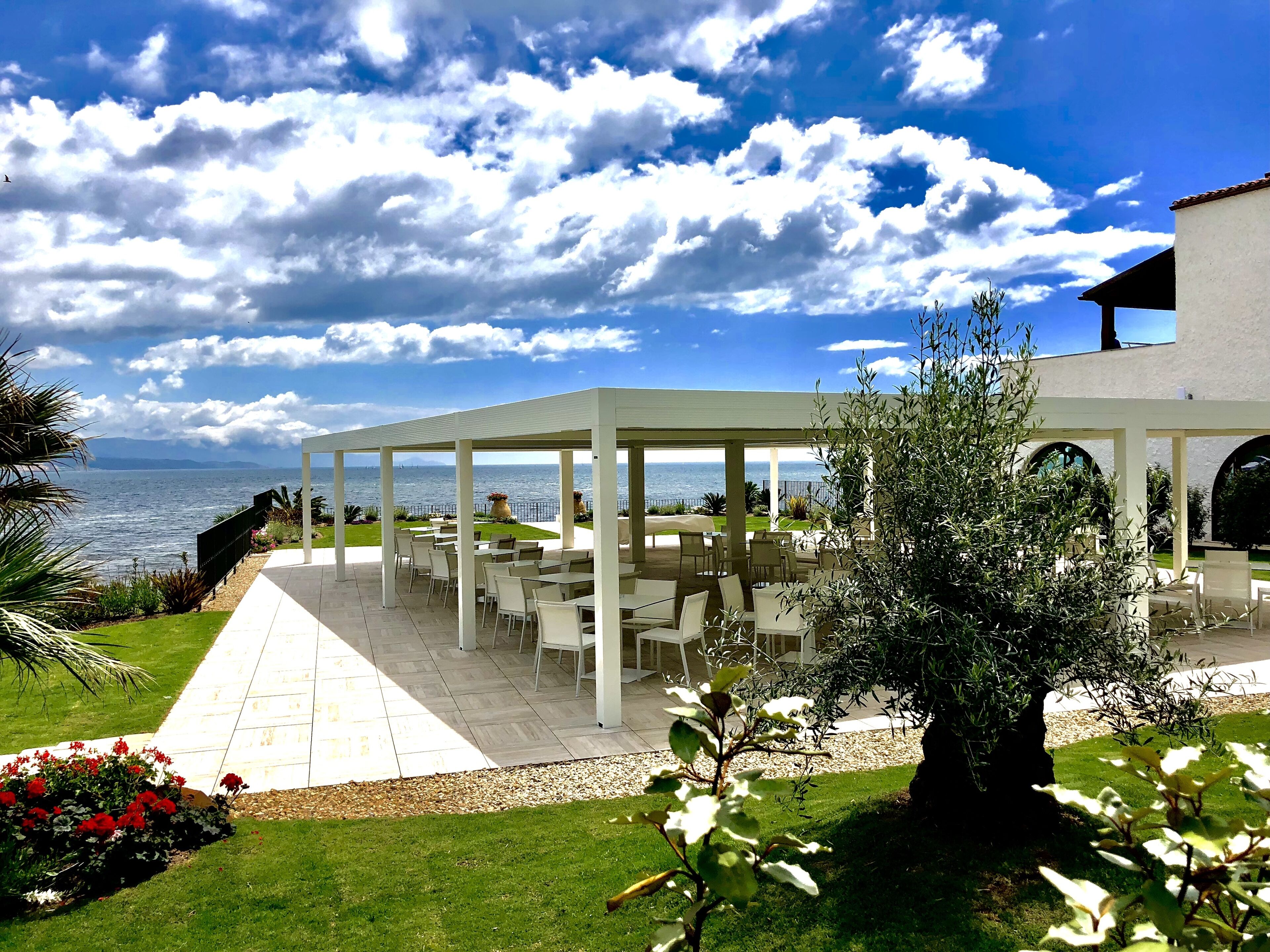 Une terrasse extérieure avec des tables et des chaises blanches, donnant sur une étendue d’eau et un ciel dégagé.