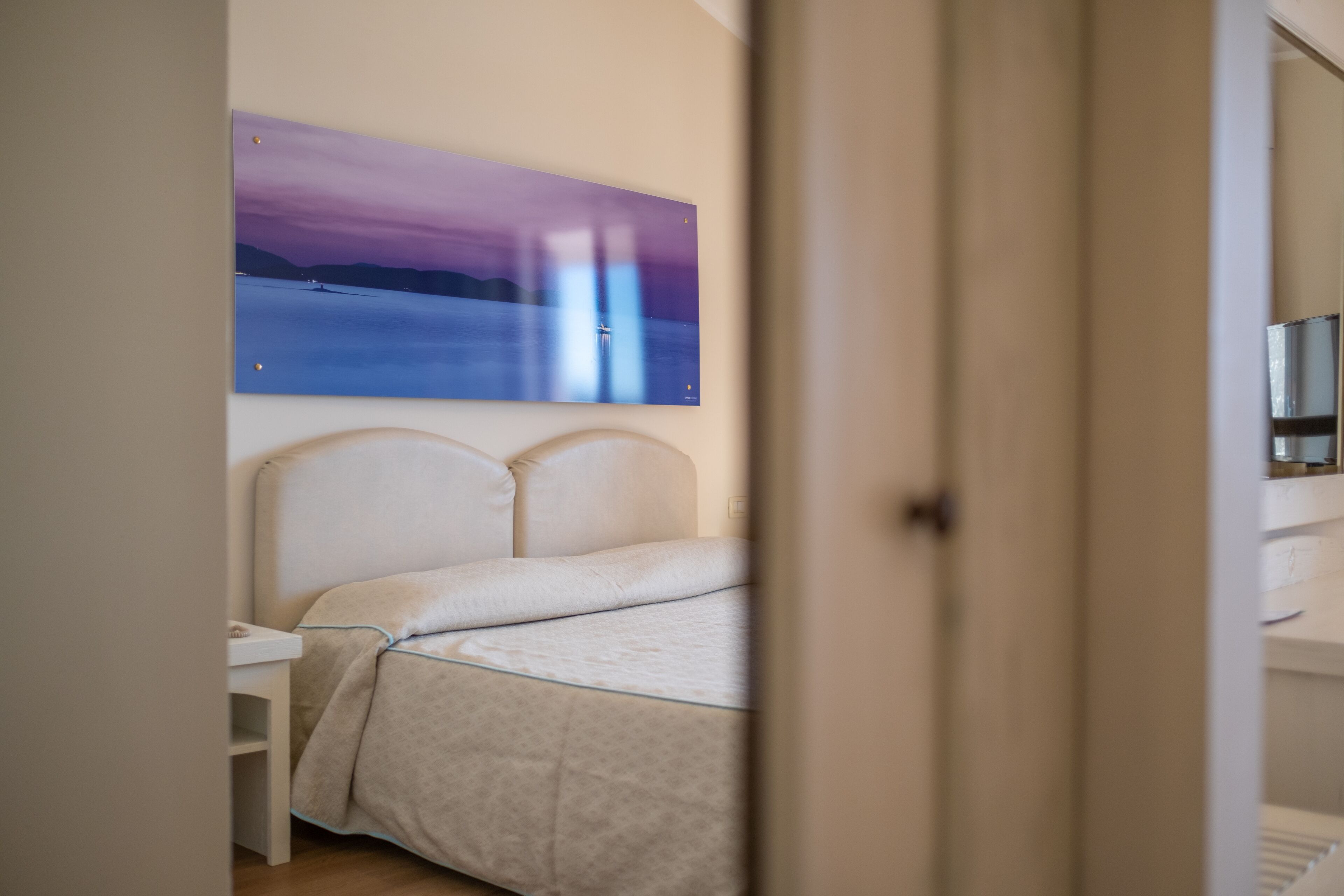 Un dormitorio con cama, mesita de noche y un cuadro de un atardecer sobre el agua en la pared.