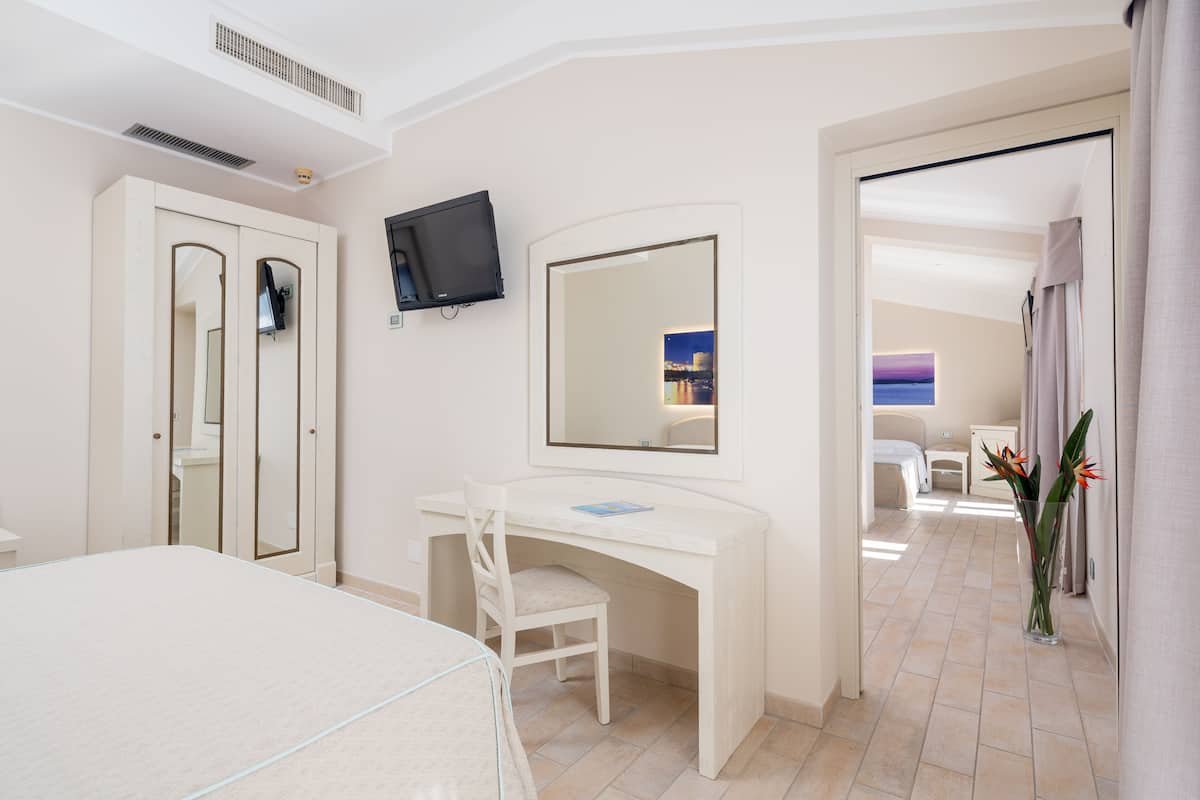 A hotel room with a bed, a desk, a chair, a TV, a mirror, and a bathroom visible through an open door.