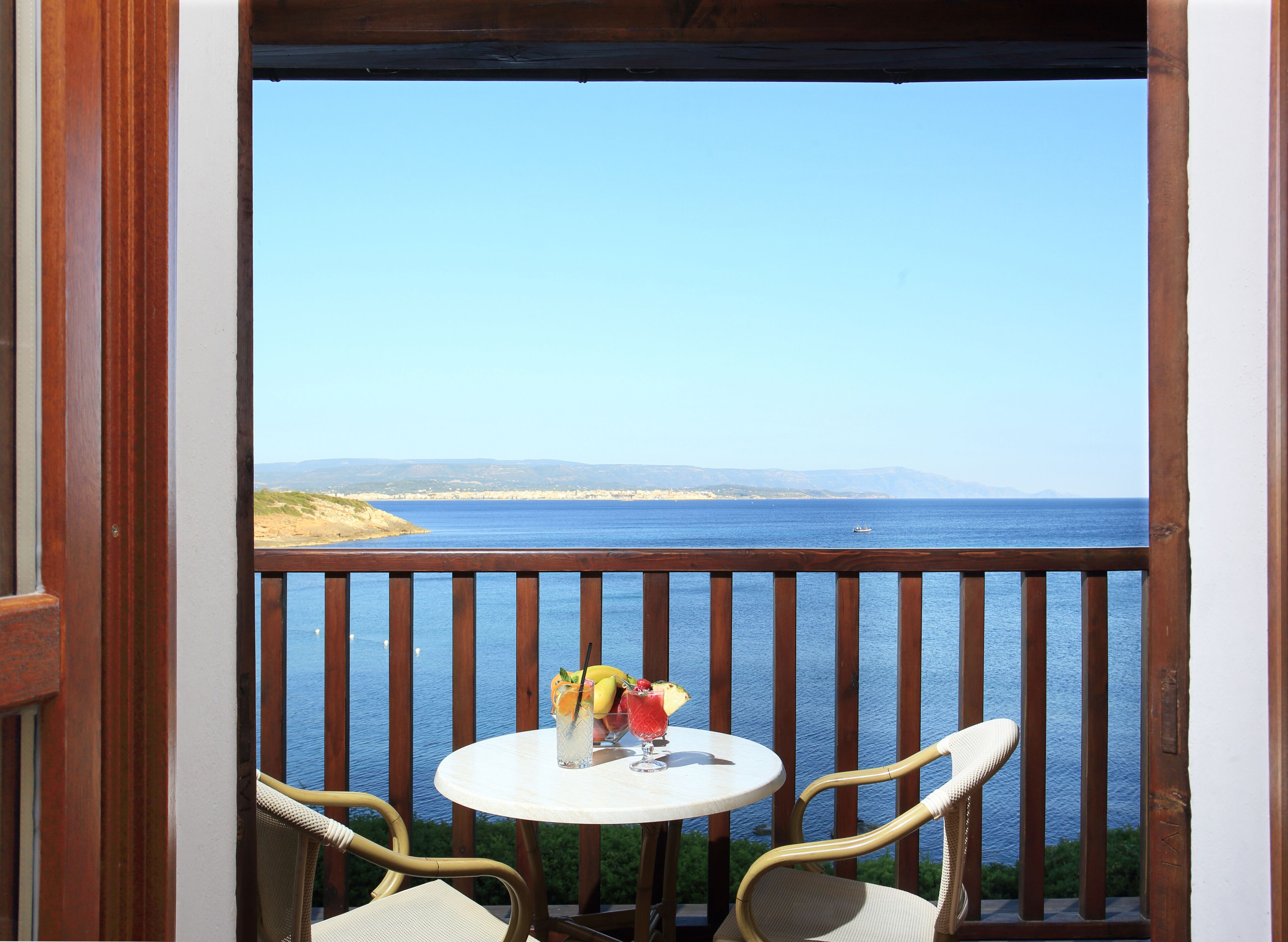 Een balkon met een tafel en stoelen, met uitzicht op een wateroppervlak en veraf gelegen land.