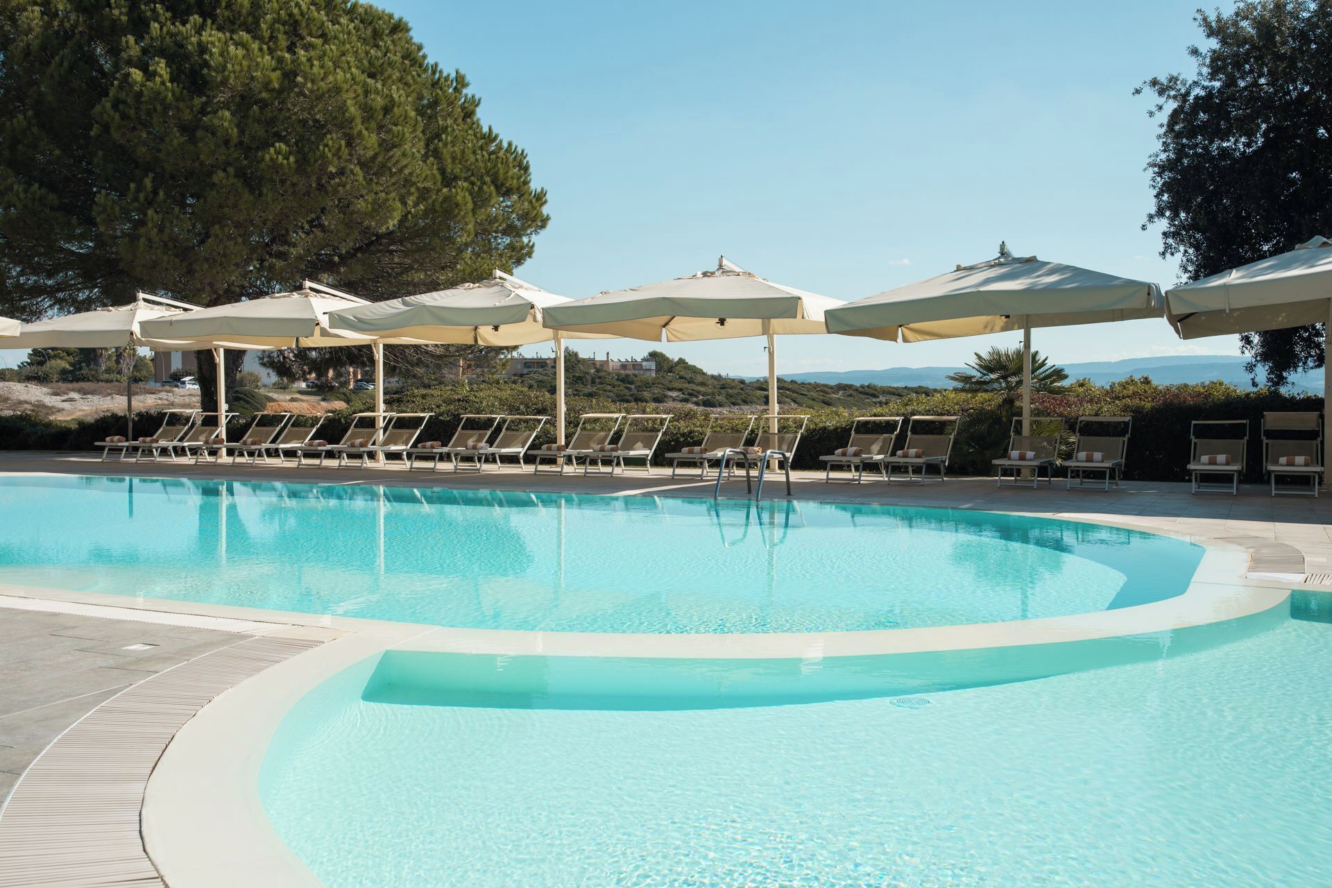 Une piscine entourée d’arbres, avec des chaises longues et des parasols, offrant une vue sur le paysage.