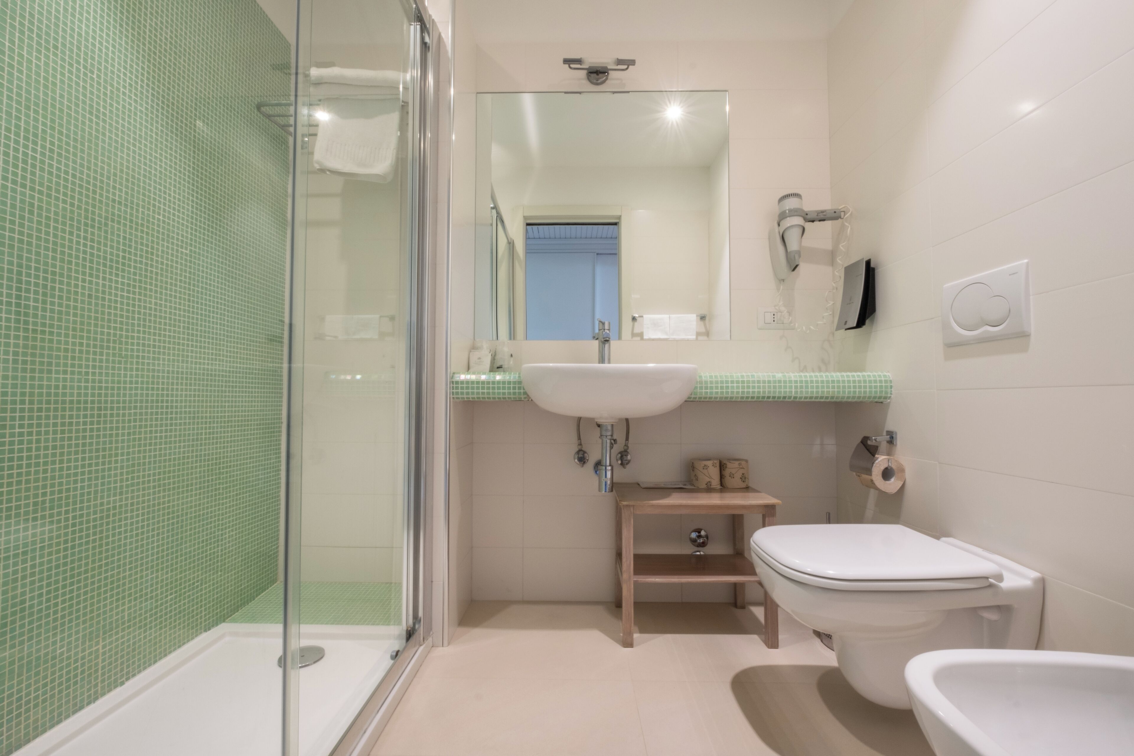 A bathroom with a glass shower enclosure, a sink, a toilet, and a bidet.
