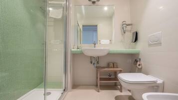 A bathroom with a glass shower enclosure, a sink, a toilet, and a bidet.