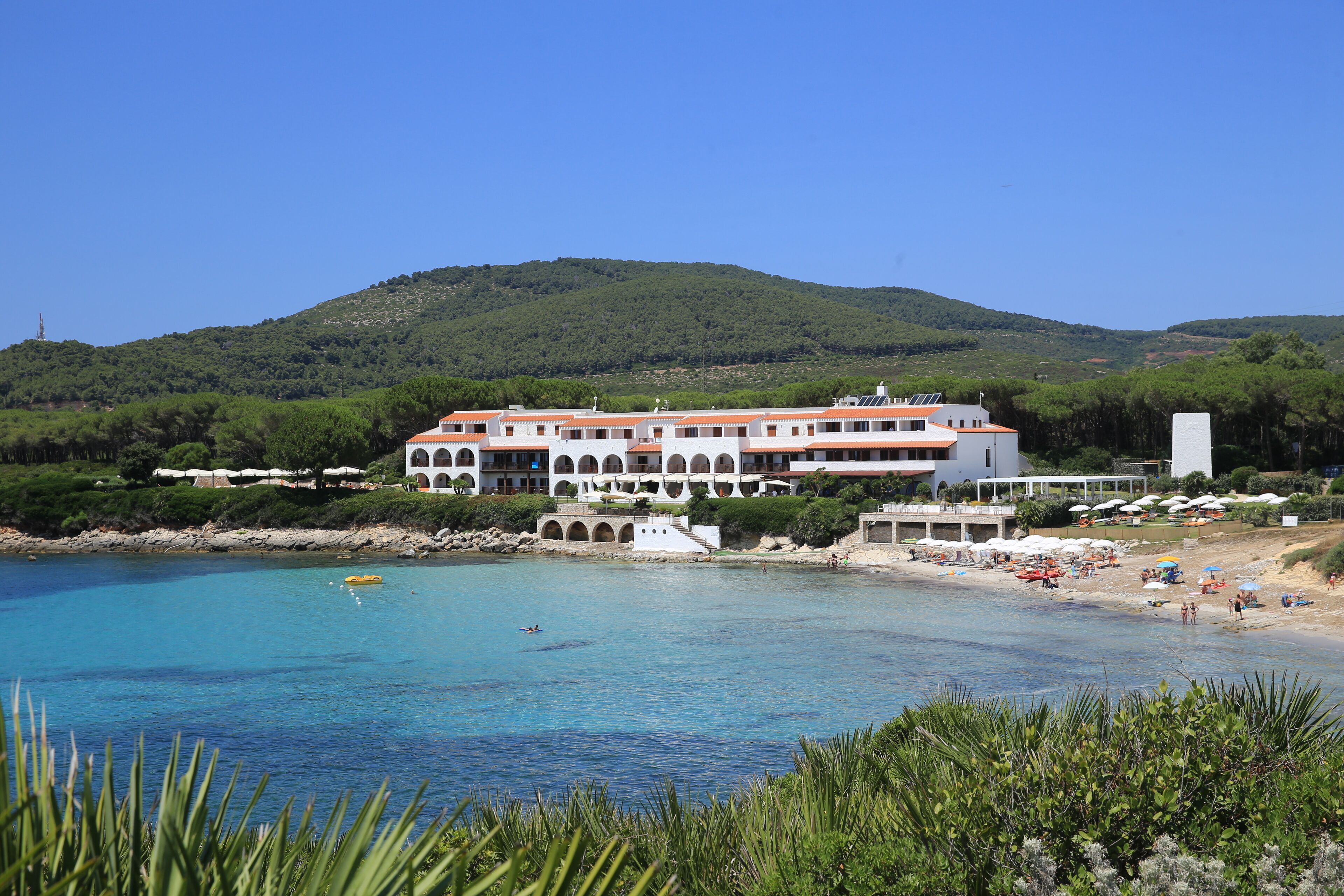 A coastal hotel with multiple balconies overlooking a beach and clear blue waters.