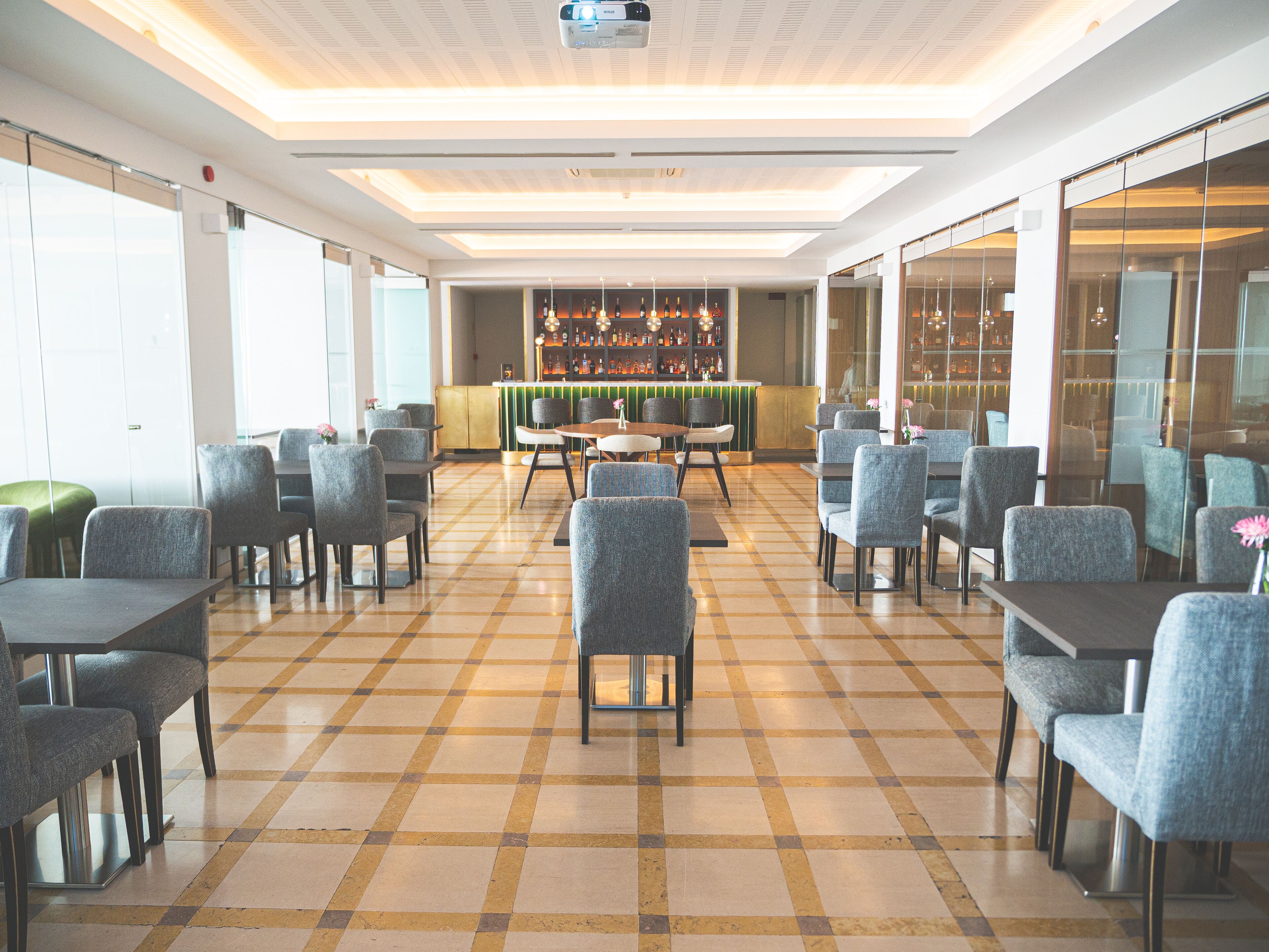 A spacious indoor area with a checkered floor, multiple seating arrangements, and a bar area with a variety of bottles.