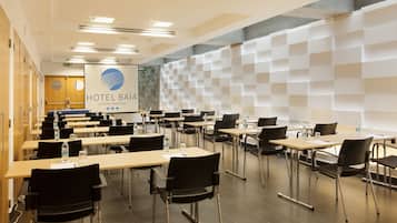Un salón de conferencias de hotel con varias mesas y sillas, una pantalla grande que muestra el nombre del hotel y un diseño de pared moderno con motivos geométricos.
