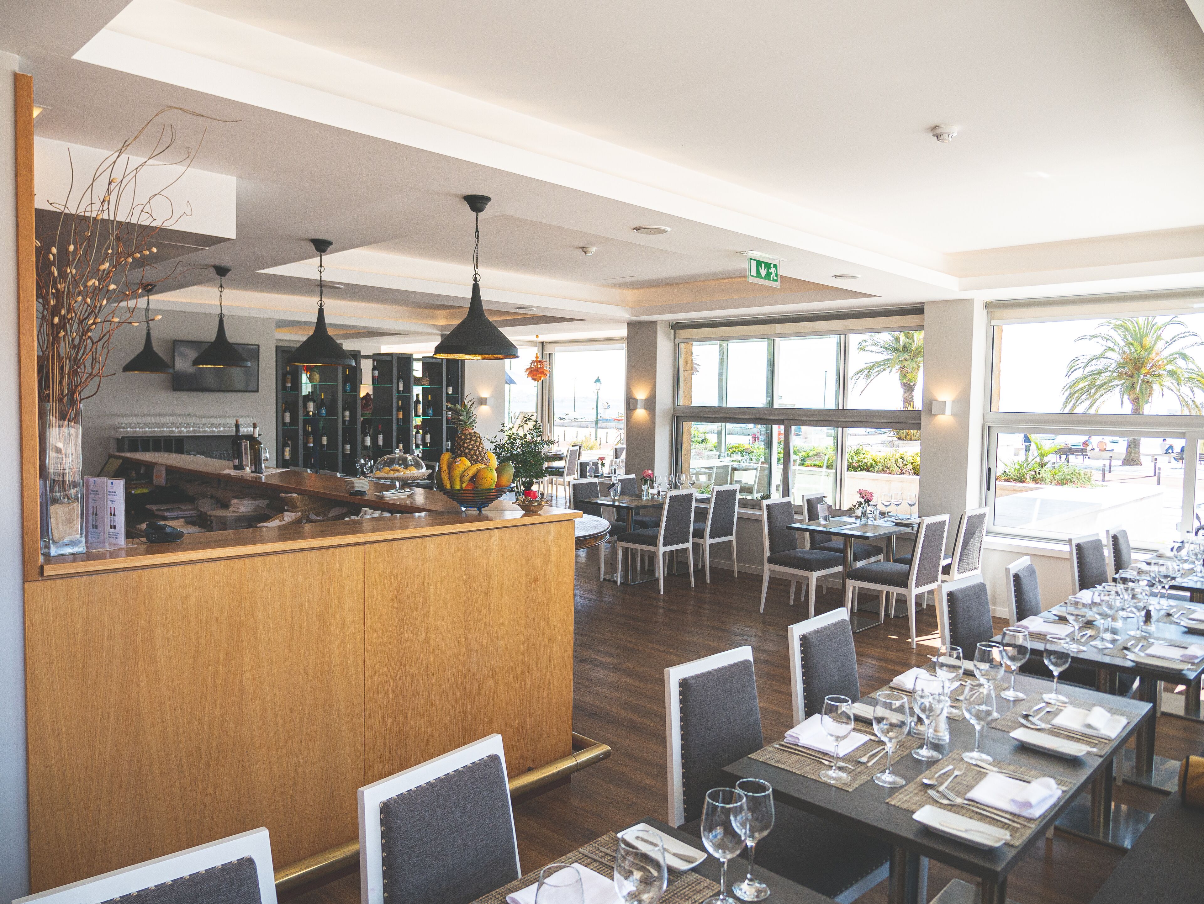 A restaurant with a wooden counter, black pendant lights, and a view of the outdoors.