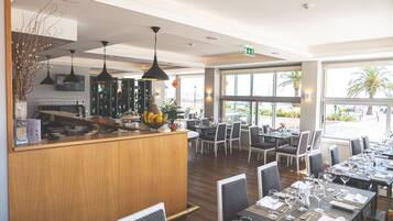 A restaurant with a wooden counter, black pendant lights, and a view of the outdoors.