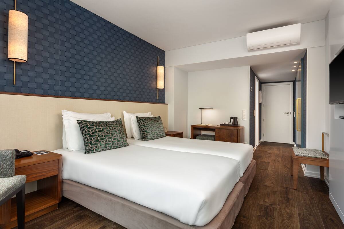 A hotel room with a large bed, two bedside tables, a desk, a chair, and a TV.
